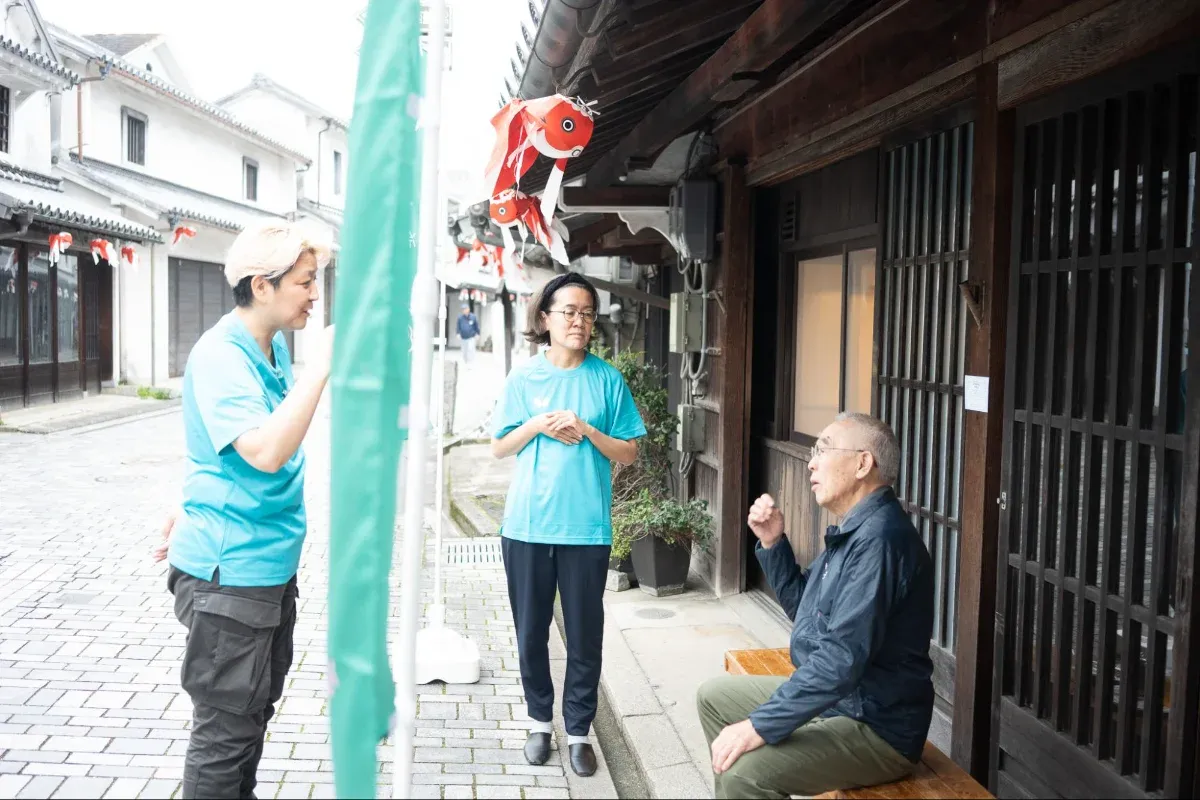 写真：ベンチに座る男性と話をする児嶋さんと話を聞く永井さん
