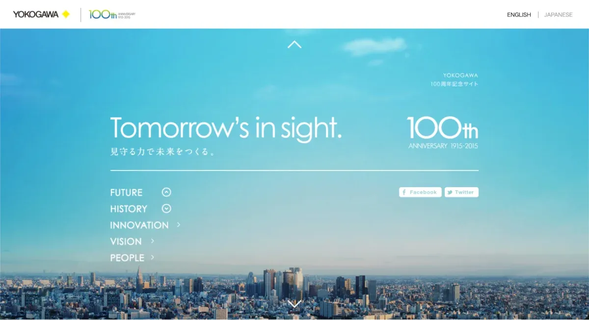 ファーストビューキャプチャ：青空と、その下に高層ビルが立ち並ぶ都市の写真が全面に配置されている。青空の前面に白いテキストが配置されている。左上に小さいテキストで「YOKOGAWA 100周年記念サイト」。中央に大きいテキストで「Tomorrow's in sight. 見守る力で未来をつくる。100th ANNIVERSARY 1915-2015」。その下にリンクが並んでいる。「FUTURE」「HISTORY」「INNOVATION」「VISION」「PEOPLE」「Facebook」「Twitter」。
