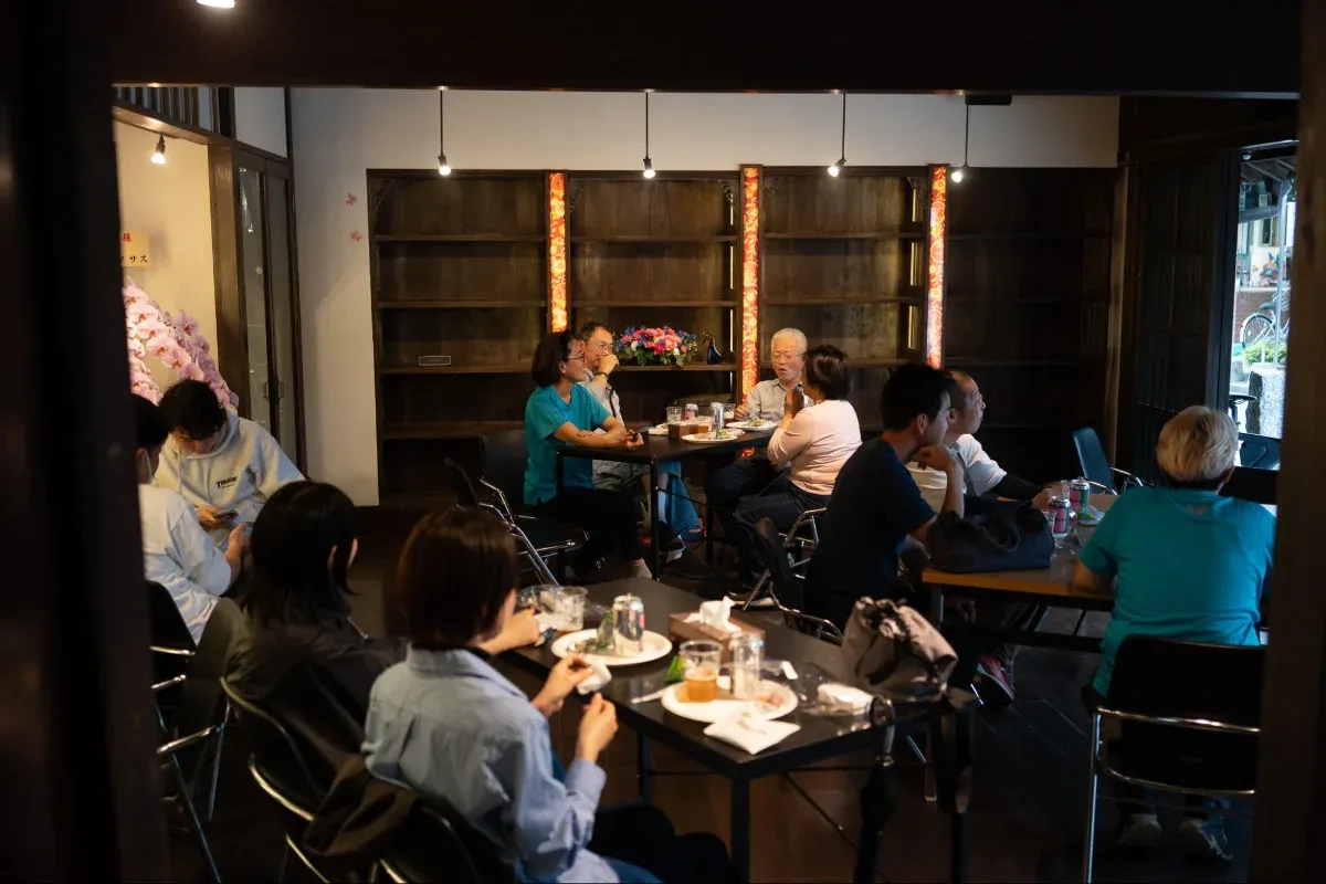 写真：古民家の中、いくつかの机を囲んでごはんやお酒を飲みながらそれぞれ自由に話をしている様子