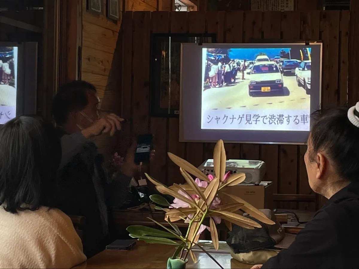 The scene shows Isao Yamada explaining using a projector, with participants listening.
