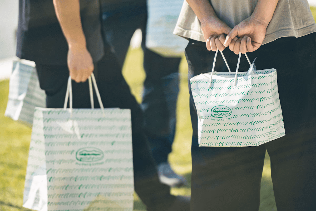 The design of the paper bag features a hand-drawn grassland on a white background.